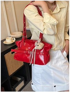 Close-up of a red pleated shoulder bag with a buckle strap and a plush teddy bear charm