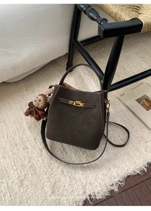 Detail of dark brown bucket bag featuring a metal twist lock and cute plush bear charm
