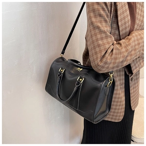 Detail of black Boston bag with gold hardware worn with a brown plaid blazer