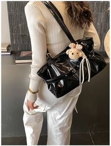 Detail of black glossy pleated tote bag with buckle and beige teddy bear charm