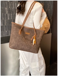 Detail of a dark brown tote bag featuring matte leather texture and brand tag