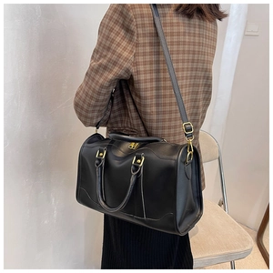 Fashionable black leather boston bag shown being worn over the shoulder by a model