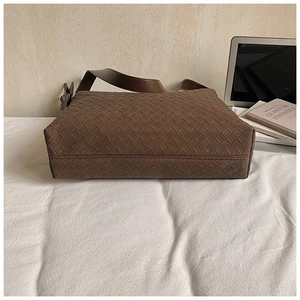 Close-up of dark brown woven leather shoulder bag with wide strap on white linen fabric