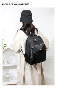 Modern black nylon backpack with gold zippers styled on a woman's shoulder in light coat