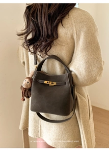 Detail of dark brown leather bucket bag featuring a gold twist lock and plush charm