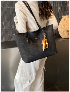 Detail of black tote bag with brand embossing and wood bead charm accessory