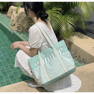 Detail of mint green canvas tote bag with large YOUNG embroidery and front pocket