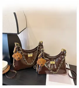 Detailaufnahme der glänzenden Hobo-Bag in Kaffeebraun mit Goldkette und Bärenanhänger