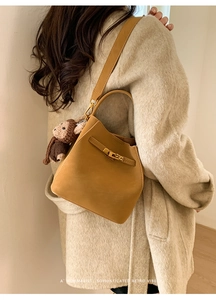Detail of mustard yellow bucket bag with gold clasp and brown monkey plush charm