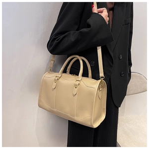 Close-up of beige leather Boston bag with gold hardware worn with a black blazer