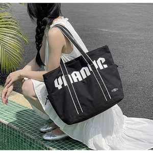 Detail of black canvas tote bag with YMAONC print and side drawstring pocket on model