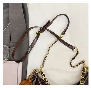 Detailansicht der dunkelbraunen Lackledertasche mit Kettenriemen und flauschigem Anhänger