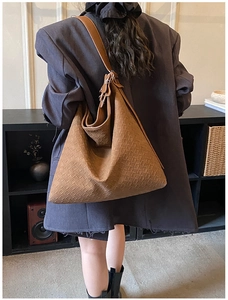 Rear view of a large brown woven leather hobo tote bag on a model in a minimalist room