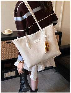 Detail of embossed cream leather tote with decorative wooden bead tassel and metal logo