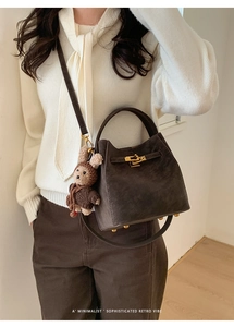 Detail of dark brown suede bucket bag with gold clasp and plush bunny charm accessory