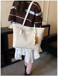 Detail of white embossed tote bag featuring leather brand tag and wood bead charm