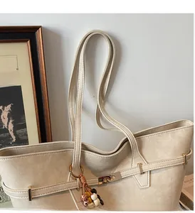 Detail of beige lychee leather tote bag featuring sturdy shoulder straps and bead charm