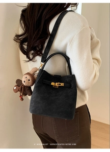 Detailed view of black suede bucket bag with gold hardware and knit animal charm