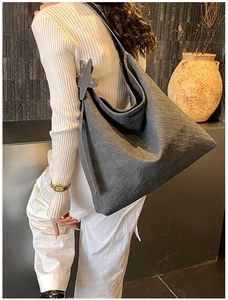 Detail of dark grey woven leather hobo bag with star pendant on metallic surface