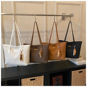 Detailed display of four suede tote bags in white, brown, and black with beaded tassels