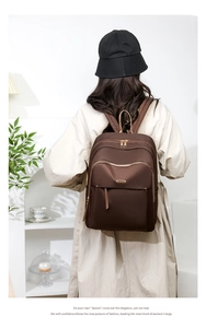Detail of dark brown oxford backpack with gold zippers and layered pockets on a female model