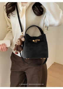 Detail of black suede bucket bag featuring golden twist lock and plush monkey charm