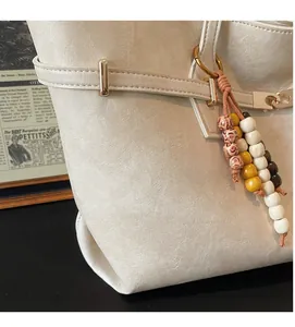 Close-up of pebble textured cream tote bag with gold buckle and beaded fringe detail