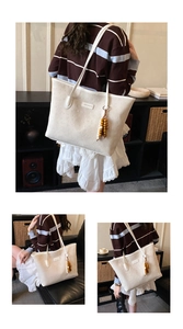 Close-up of white tote bag with logo embossing, metal plaque and wooden bead charm