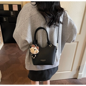 Detail of black lychee grain bucket bag featuring a cute plush bear charm with bowknot
