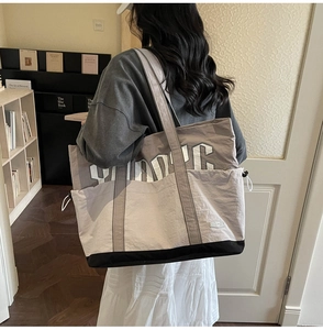 Detail of a large color-block tote bag with drawstring side and white letter design