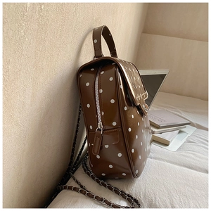Polka dot brown leather backpack with chain strap resting against books on a desk