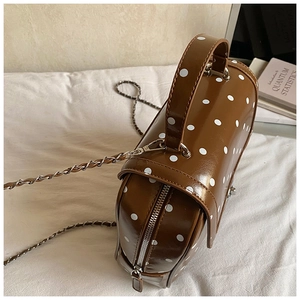 Close-up of a coffee brown polka dot cylinder bag with chain strap and silver zipper