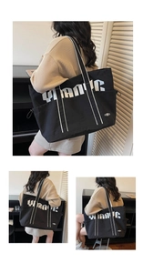 Close-up of large black canvas tote bag with white letter print and striped strap