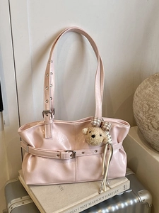 Pink glossy tote bag with buckle straps and teddy bear charm on a silver suitcase