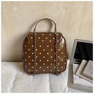Detail of a brown polka dot backpack with silver chain straps and a glossy PU leather finish