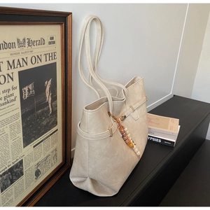Detailed shot of beige tote bag featuring pebbled leather texture and colorful beaded charm