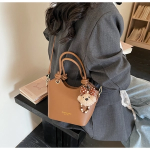 Brown lychee leather bucket bag with gold logo, teddy bear charm, and shoulder strap detail
