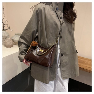 Details einer dunkelbraunen Lackledertasche mit goldenem Drehverschluss und Bärenanhänger