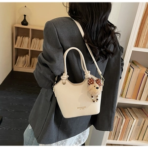 Close-up of beige lychee pattern leather tote bag with knotted handles and a cute bear charm