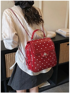 Detail of red polka dot backpack with silver clasp and chain strap worn by a model