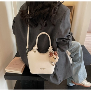Close-up of beige litchi grain bucket bag with cute bear charm and twisted handle