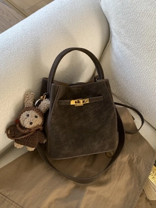 Deep brown matte leather bucket bag with gold clasp and plush bear charm on white sofa