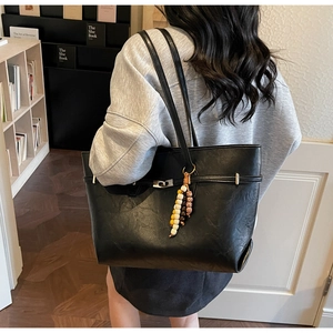 Close-up of black textured faux leather tote bag with colorful bead charm on a model
