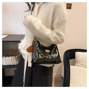 Detail der schwarzen Lackhandtasche mit goldener Kette und braunem Bärenanhänger