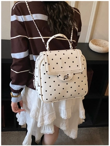 Close-up of white polka dot backpack featuring silver metal twist lock and chain strap