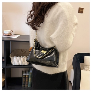 Details einer glänzenden schwarzen Lackleder-Schultertasche mit goldener Kette
