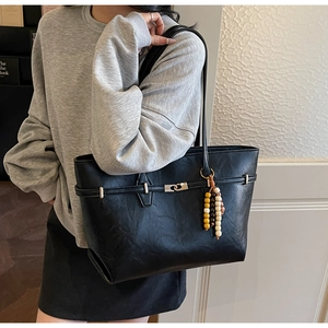 Detail of black tote bag featuring metal buckle strap and colorful beaded tassel pendant