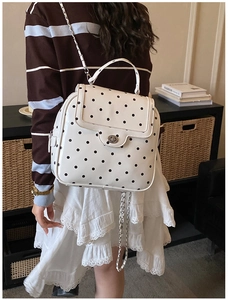 Detail of white leather backpack with black polka dots and silver chain straps on a model