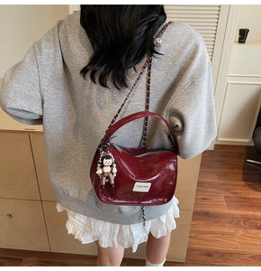 Détail d'un sac à main rouge vin brillant avec bandoulière chaîne et pendentif cartoon