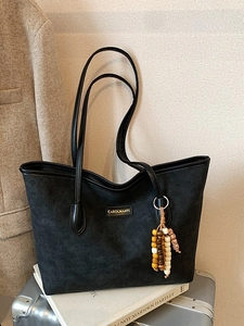 Large black textured tote bag with heart pattern and beaded charm on suitcase